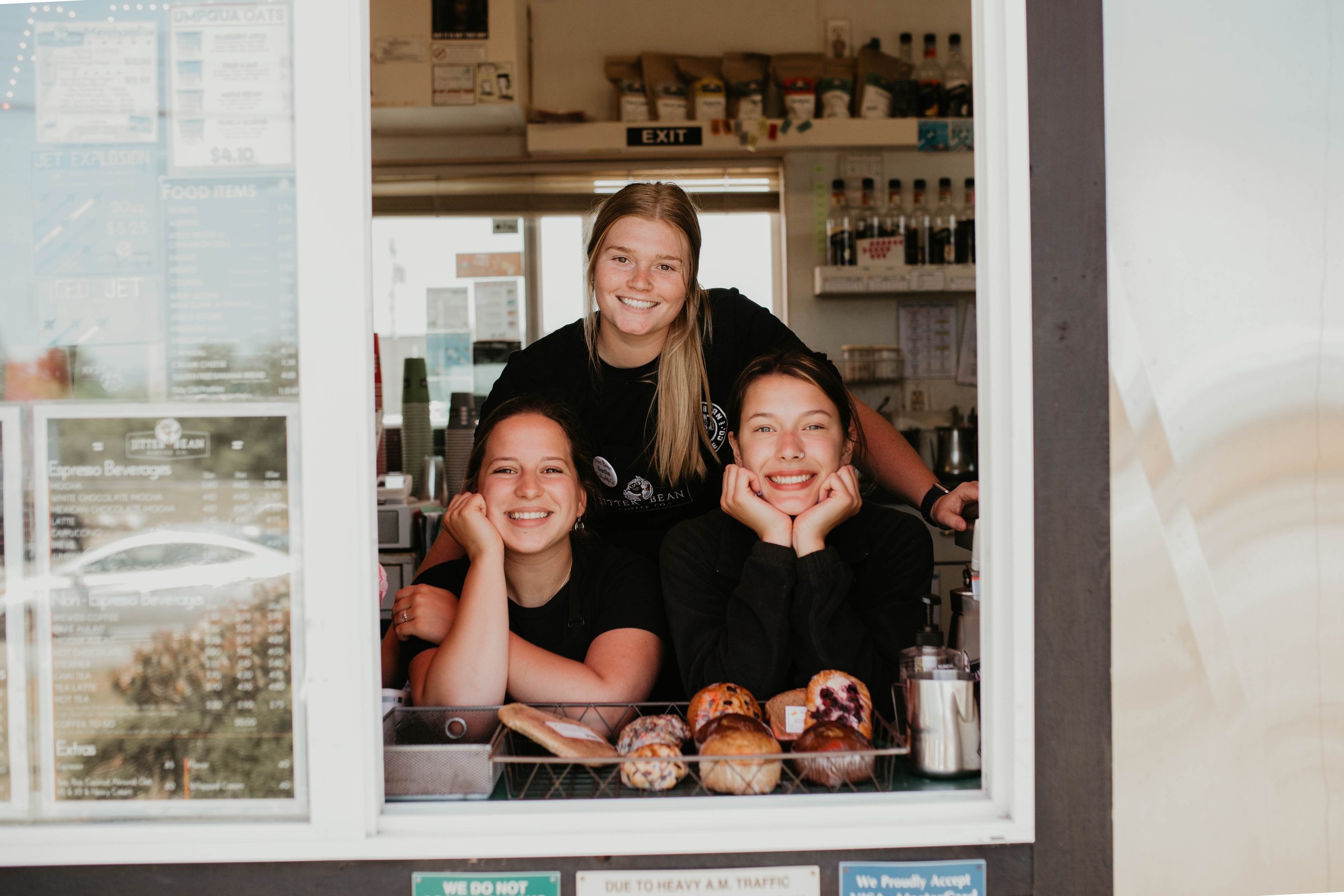 Three Jitter Bean baristas leaning out of a drive-thru window
