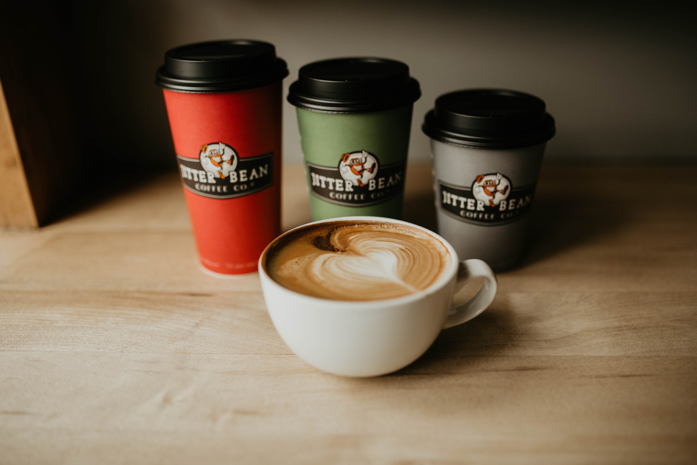Three Jitter Bean to-go cups beside a latte in a white cup